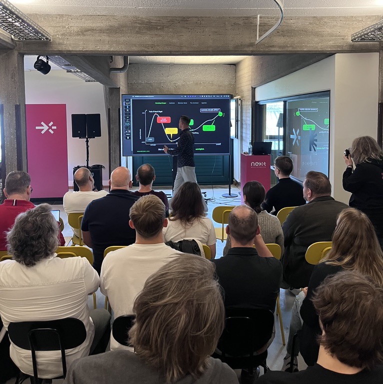 Community-Event: Vortrag vor einem großen Bildschirm, Mitglieder sitzen in Reihen davor