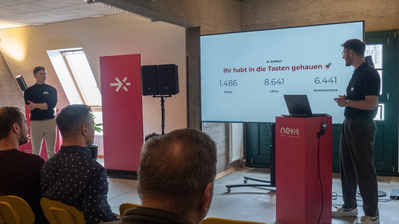 Community-Event: Vortrag mit den Community-Zahlen auf dem Bildschirm, davor sitzen Mitglieder